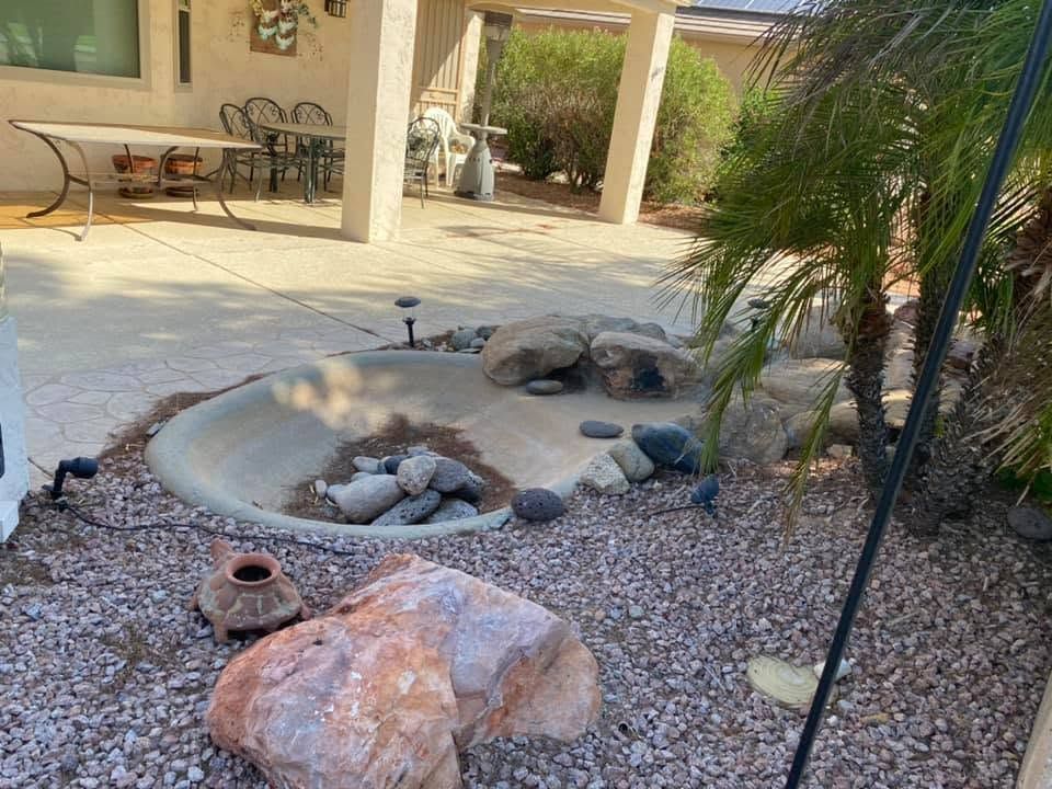 Desert garden with a dry rock pond, large boulders, gravel, and a patio seating area in the background