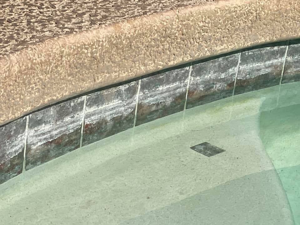 Empty pool with pale green water and a stone edge below a gravel path