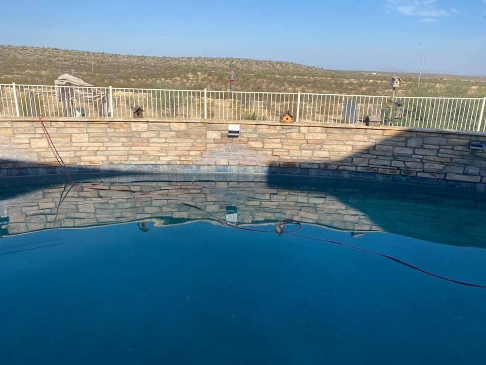 Swimming pool with blue water, stone wall, and hillside view under clear sky