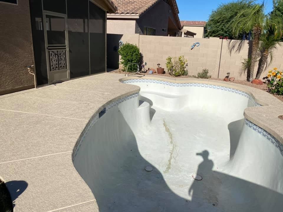 Empty in-ground pool with beige decking and a stucco backyard wall in bright sunlight