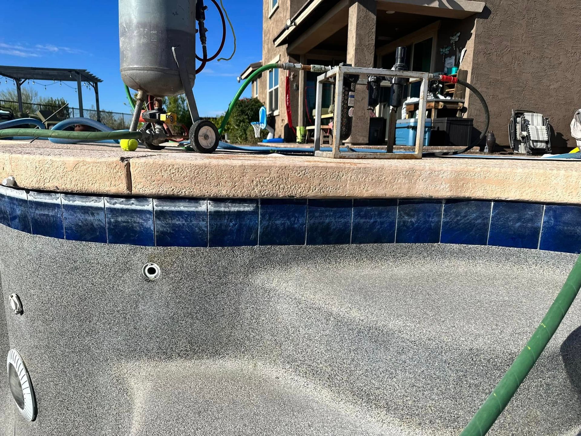 In-ground pool edge with blue tile, concrete deck, and pool equipment beside a house