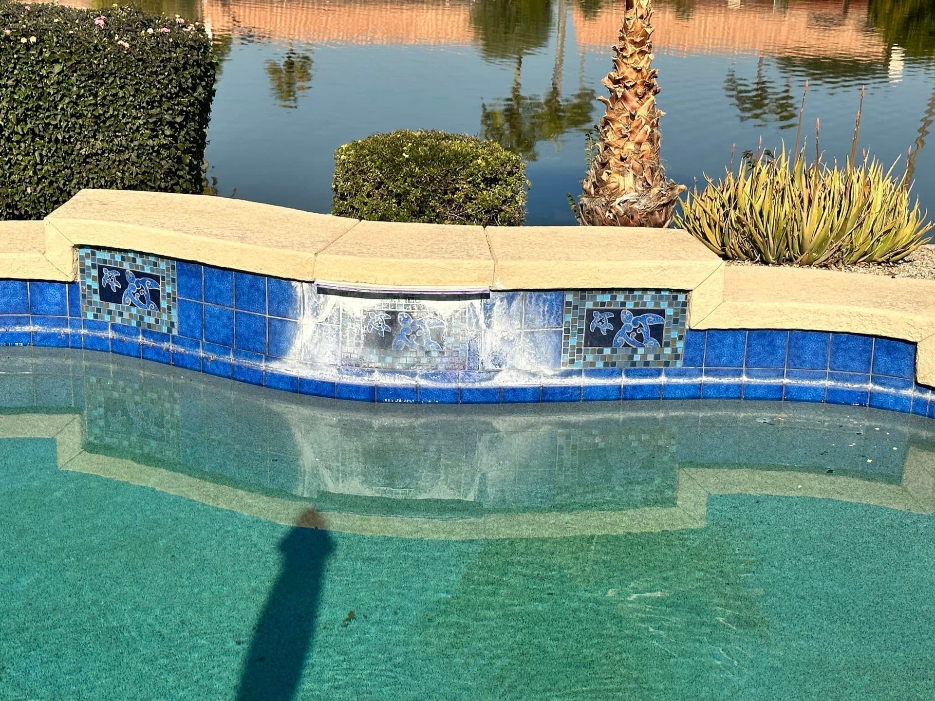 Blue-tiled backyard pool waterfall with tan coping and palm trees in the background