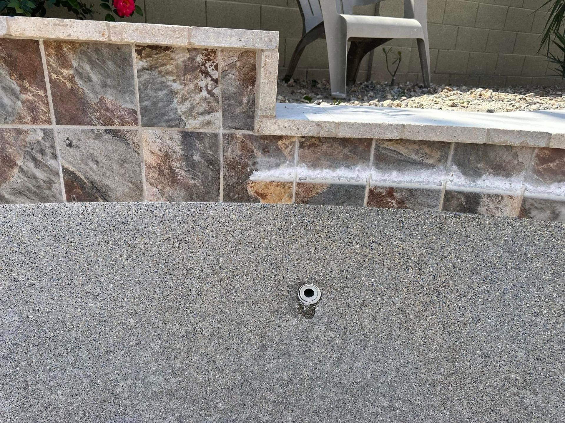 Stone retaining wall with a small outlet or pipe above a gray textured surface