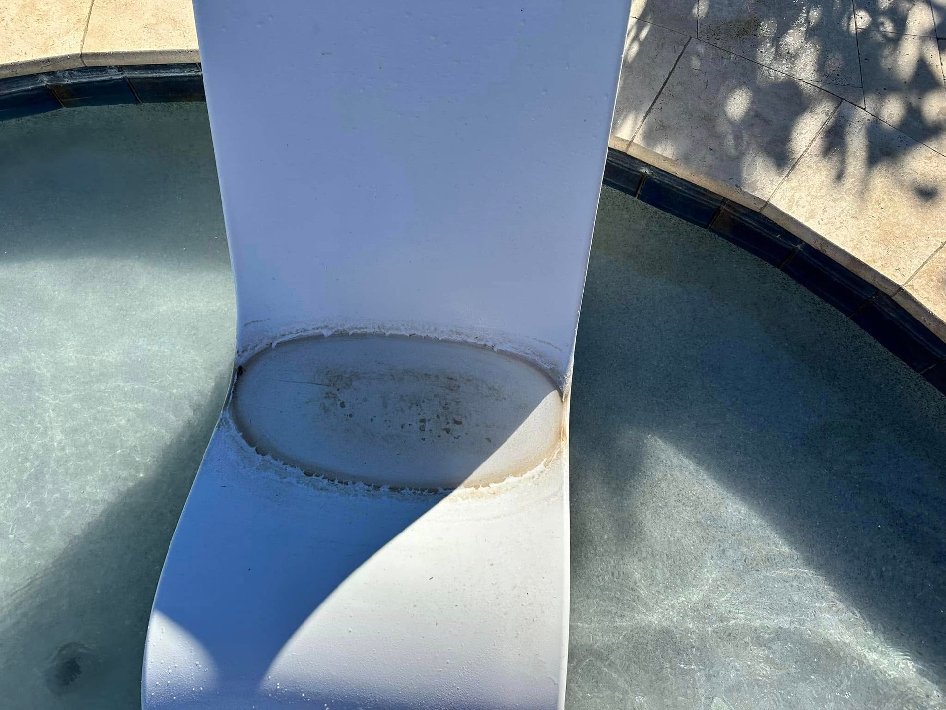 Close-up of a white pole in a round fountain basin with greenish water and shadows