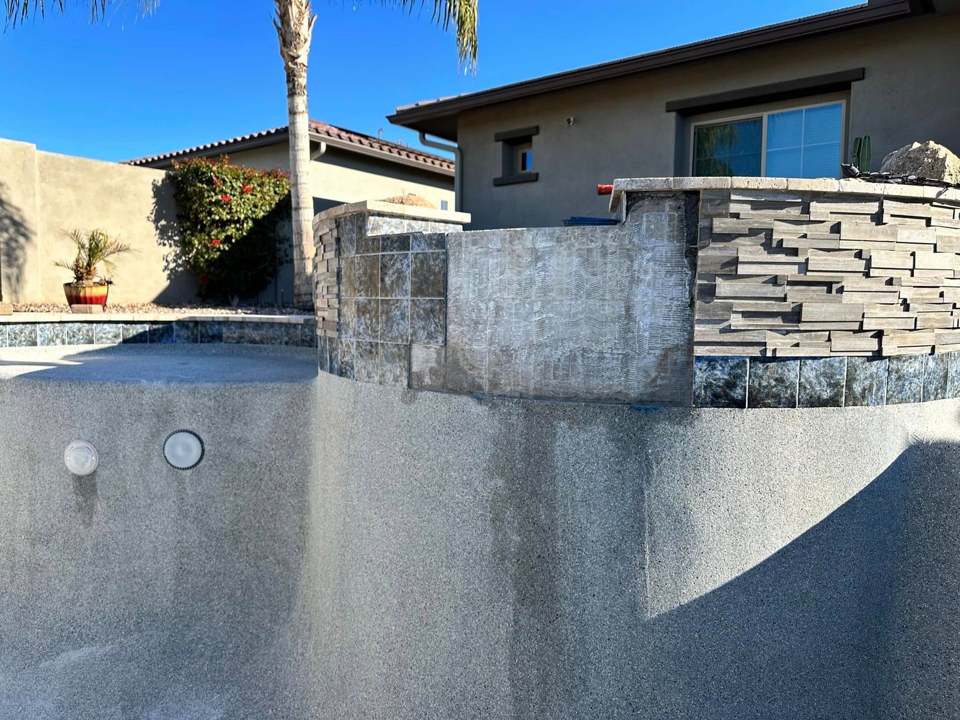 Empty backyard pool with gray stucco walls and a modern house in the background.