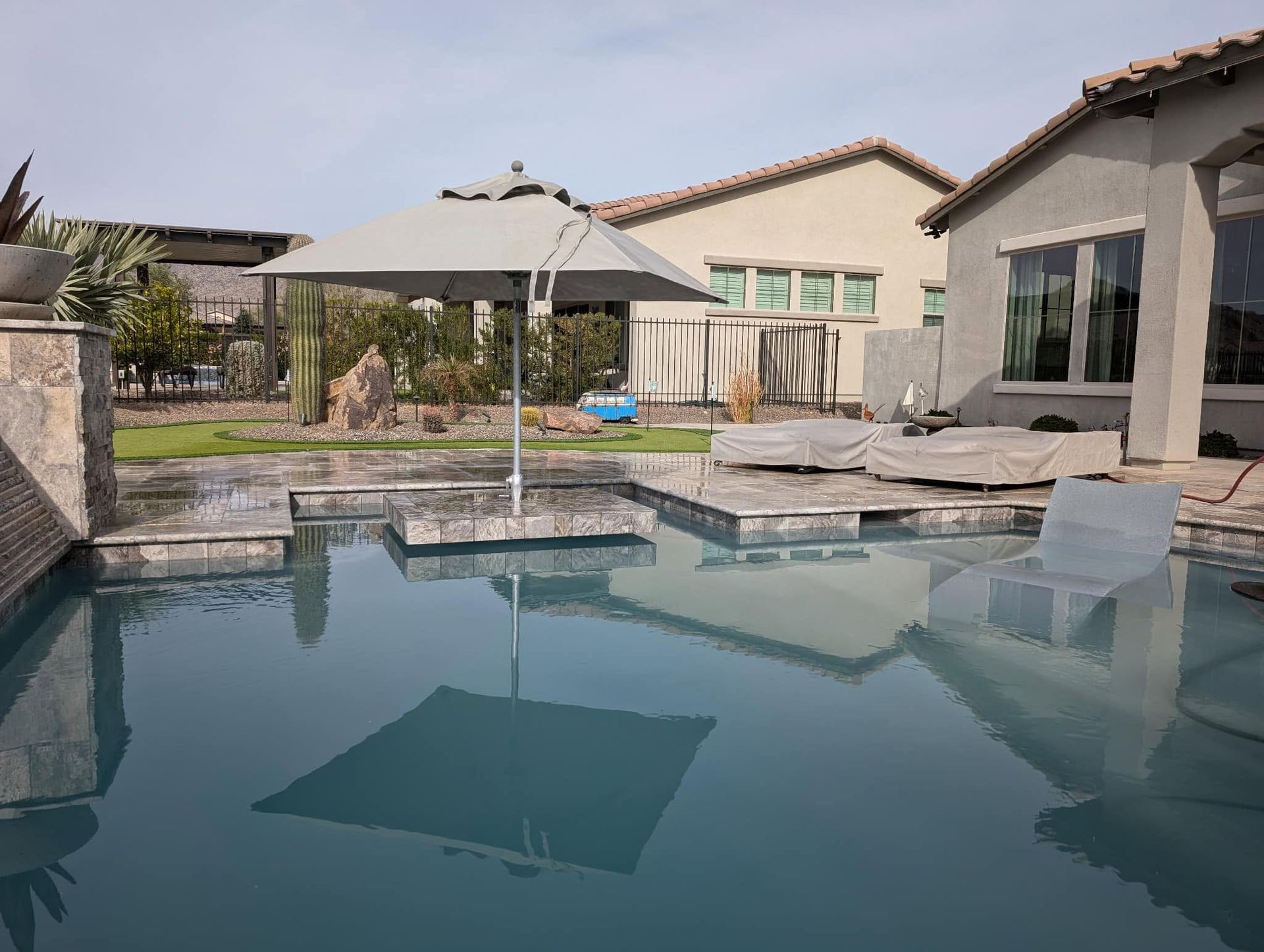 Backyard pool with loungers, umbrellas, and a patio beside a modern house