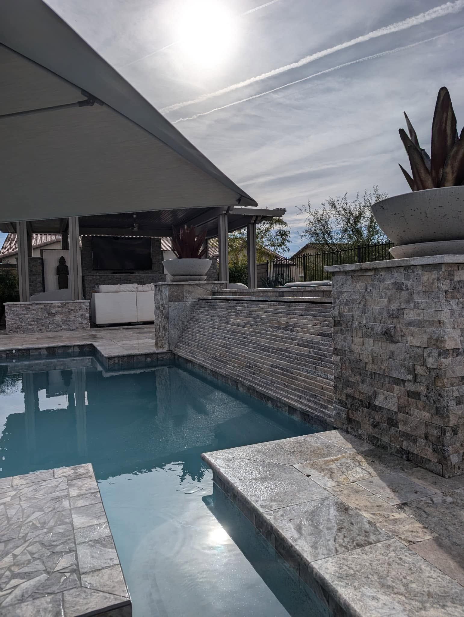 Stone-tiled pool with water feature under a canopy in a sunny outdoor patio area