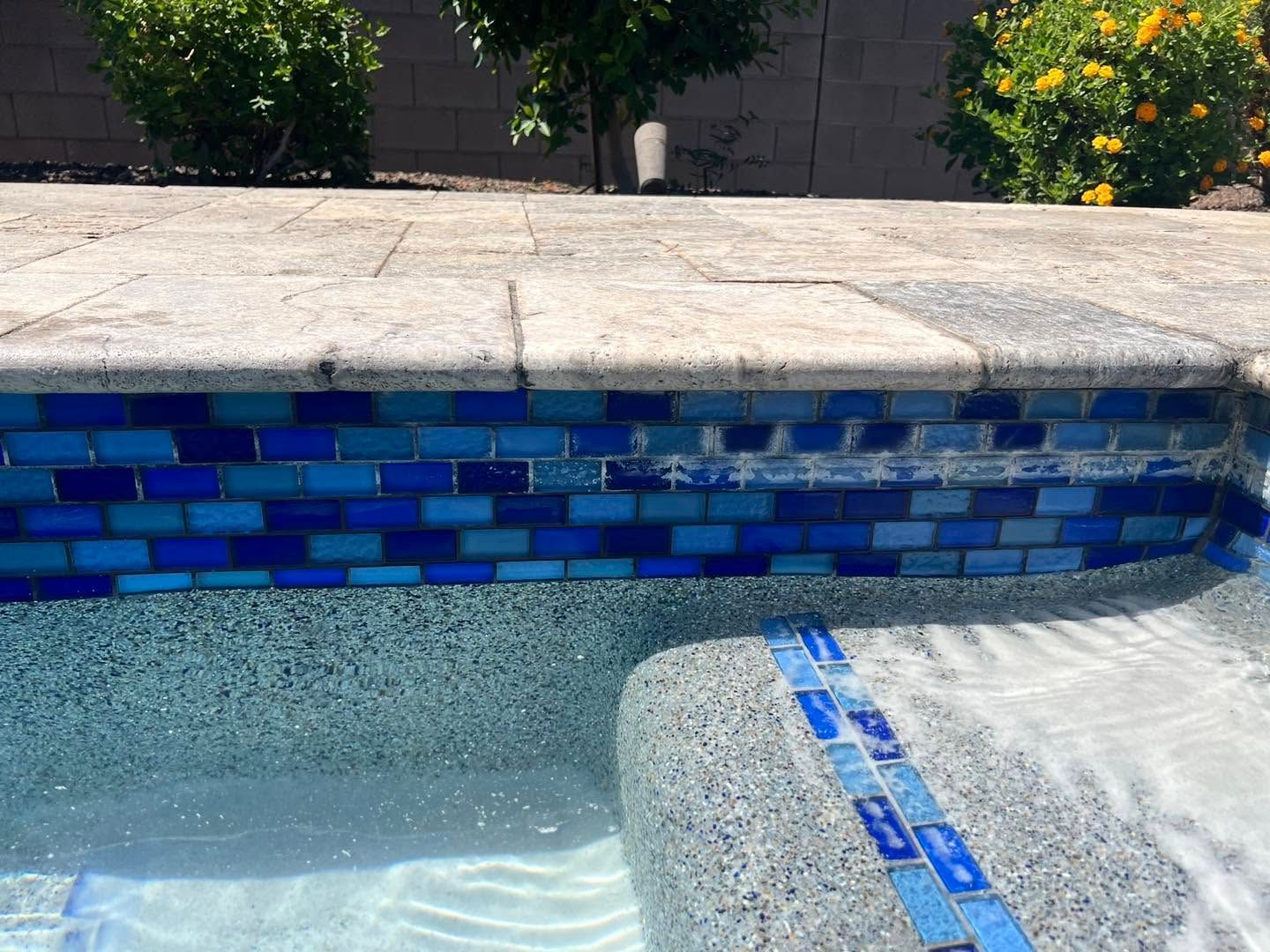 Empty tiled swimming pool with blue mosaic coping and shallow water flowing over a ledge