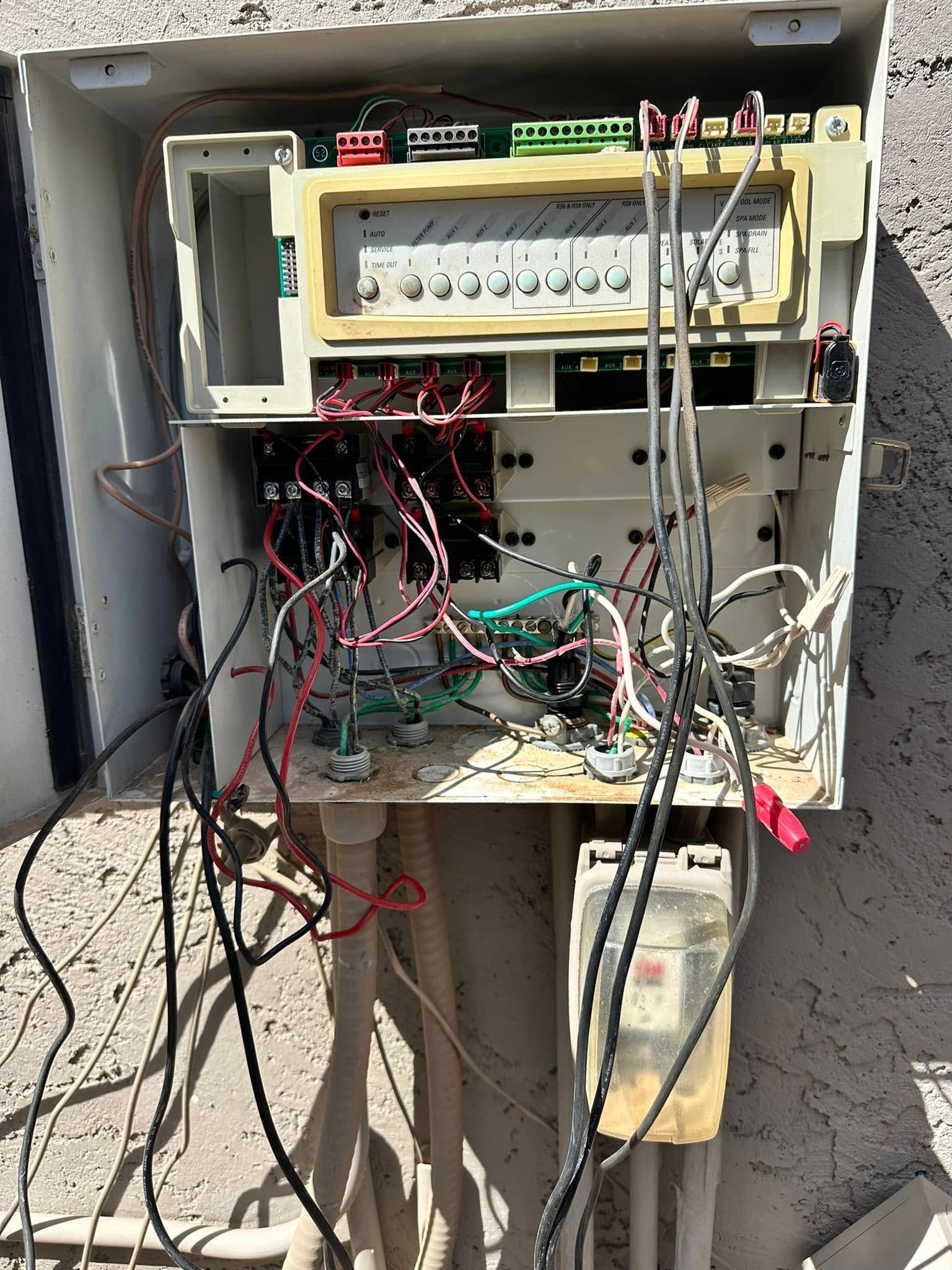 Open electrical service panel with tangled wires and exposed components outdoors