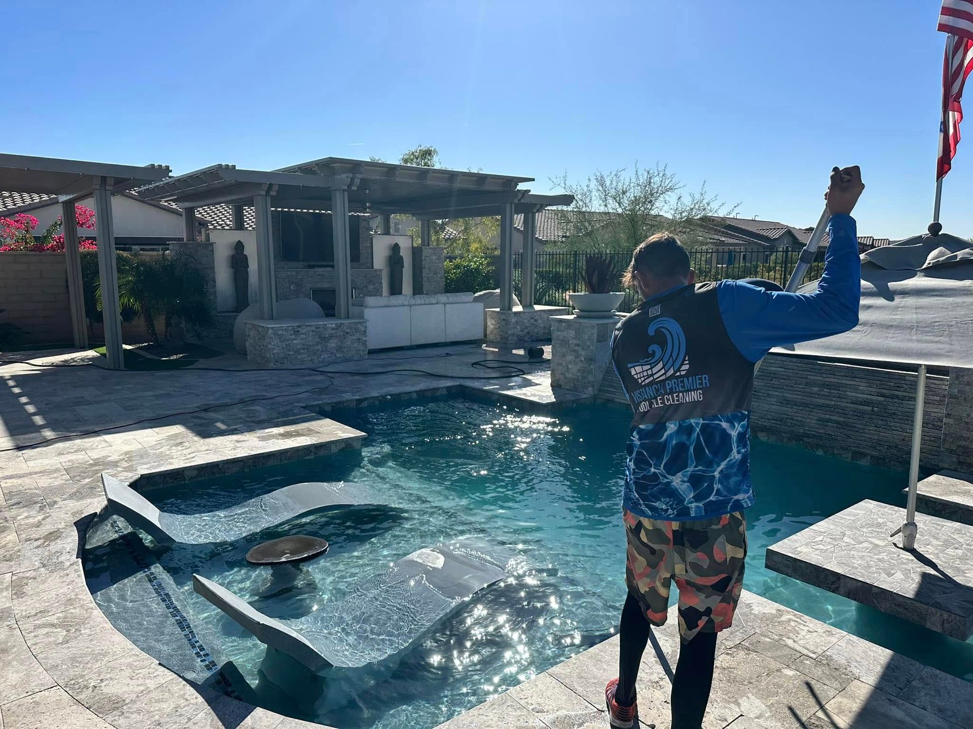 Person standing at the edge of a pool, holding a fishing rod near floating objects on the water