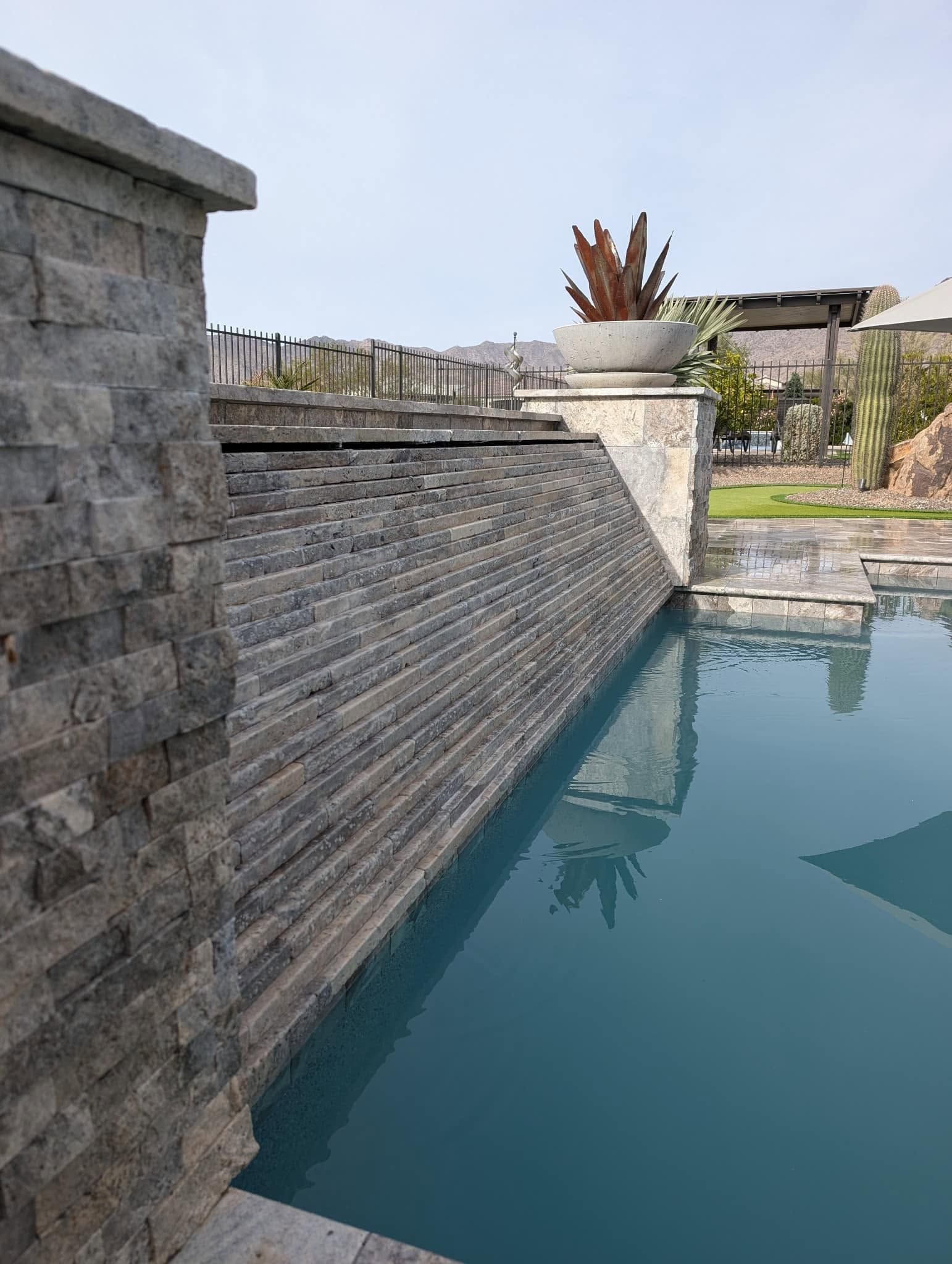 Stone pool wall beside calm blue water under a clear sky