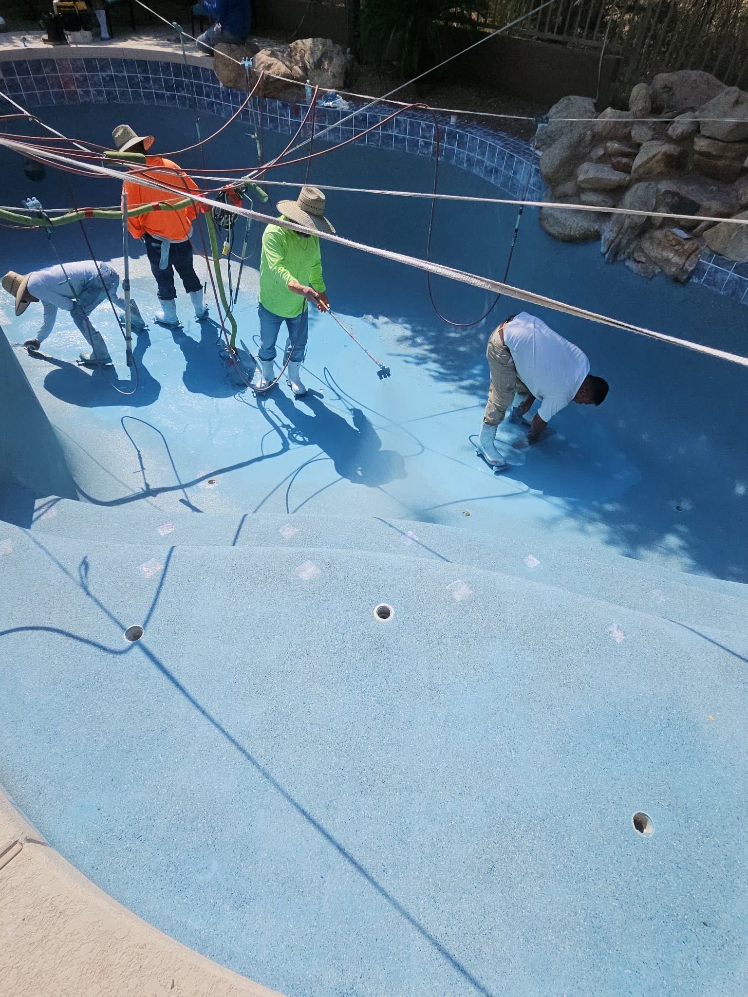 Children playing in a dry blue fountain, climbing and crouching near ropes and rocks