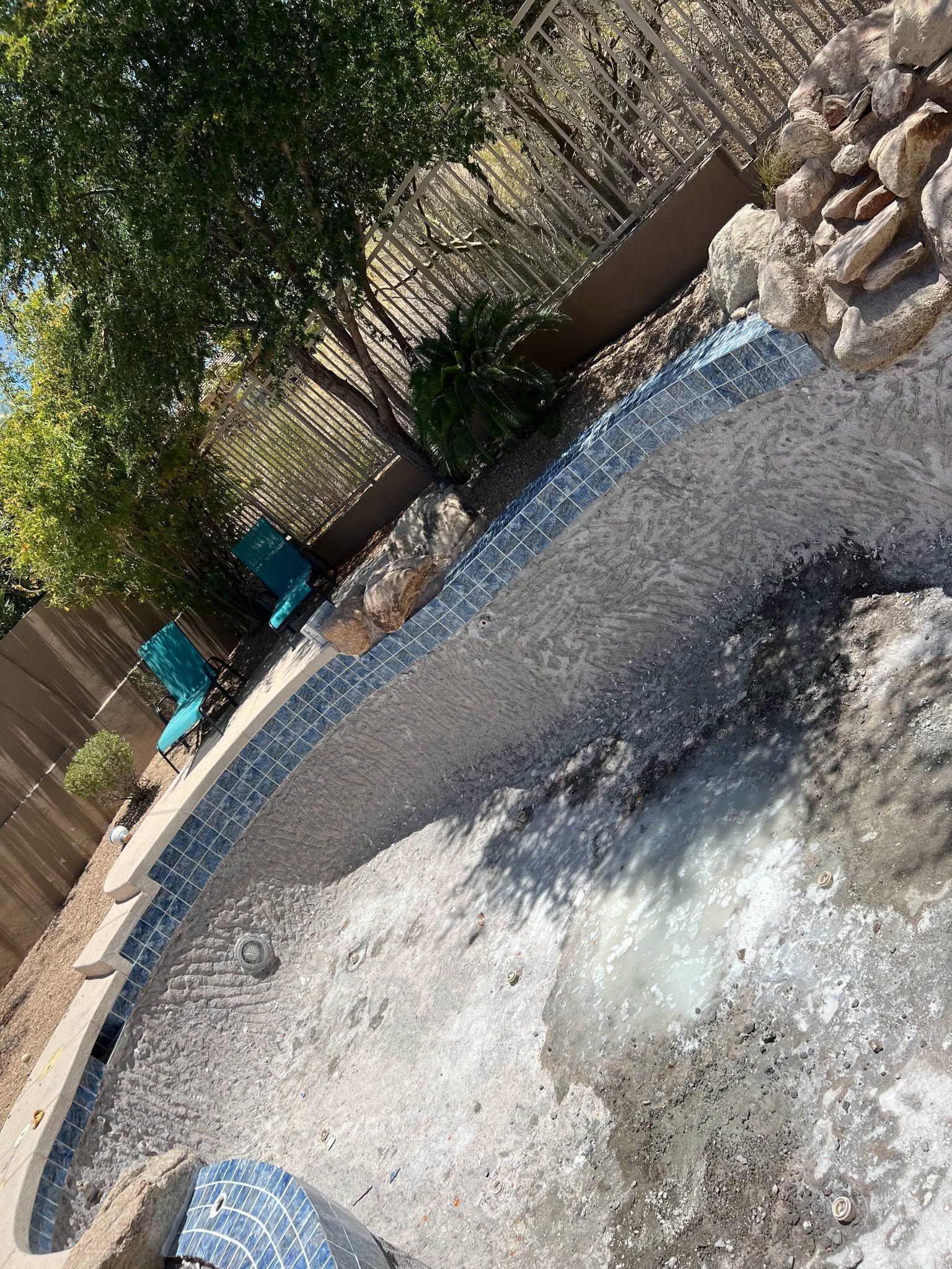 Backyard pool with blue lounge chairs, trees, and gravel around the waterline