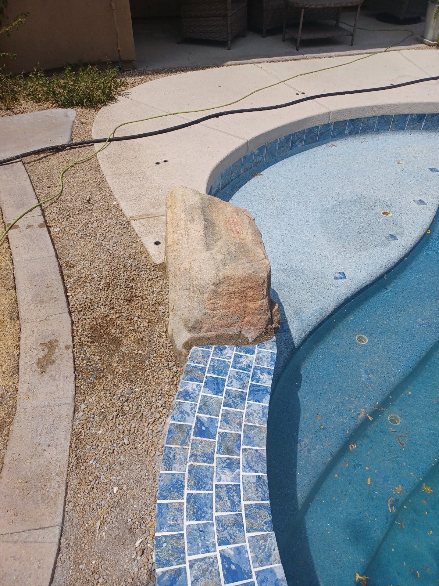 Pool edge with blue tile trim, a tan stone block, and curved concrete deck beside water
