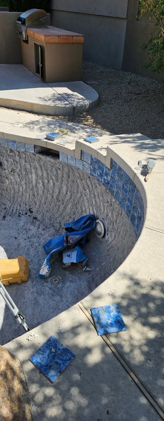 Empty concrete pool with a blue bag and scattered debris, viewed from above.