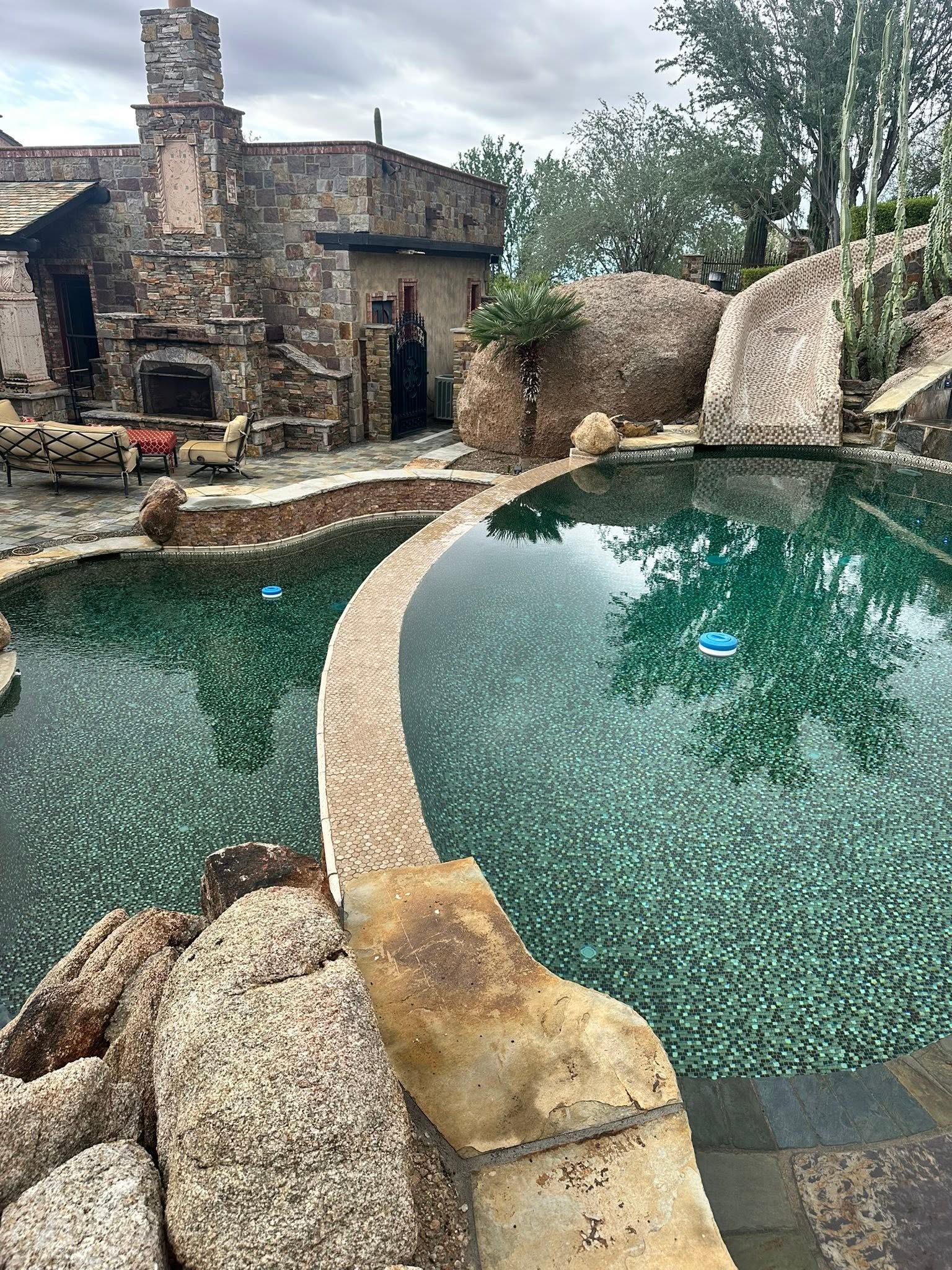 Stone courtyard with a turquoise pool beside an old rustic building and trees.