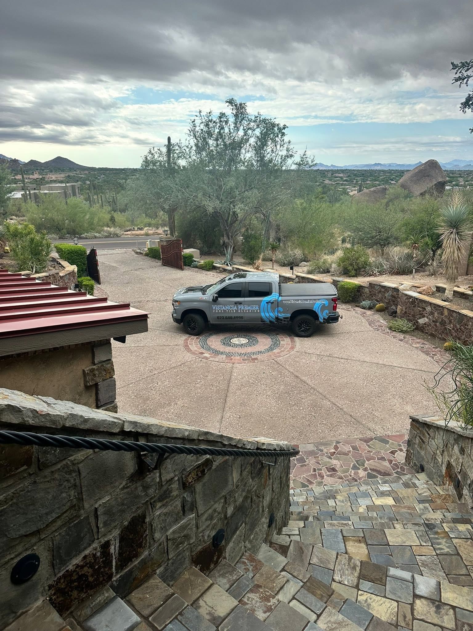 Blue pickup truck parked in a gravel driveway beside stone walls and desert landscaping under cloudy skies
