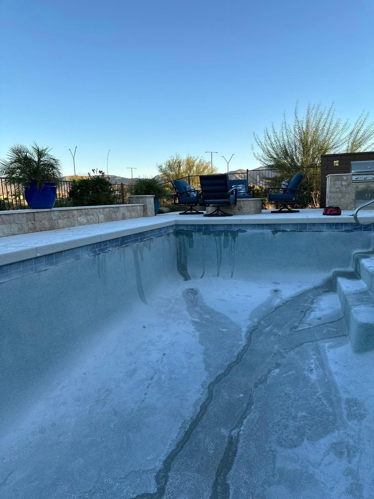Empty drained swimming pool with blue sky and outdoor patio in the background