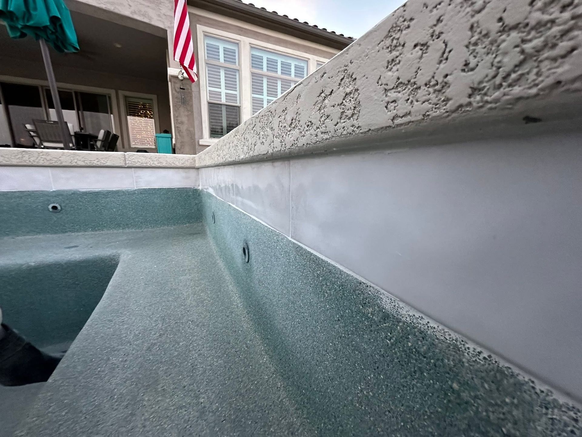 Empty pool or spa interior with pale blue speckled walls and a house patio above.