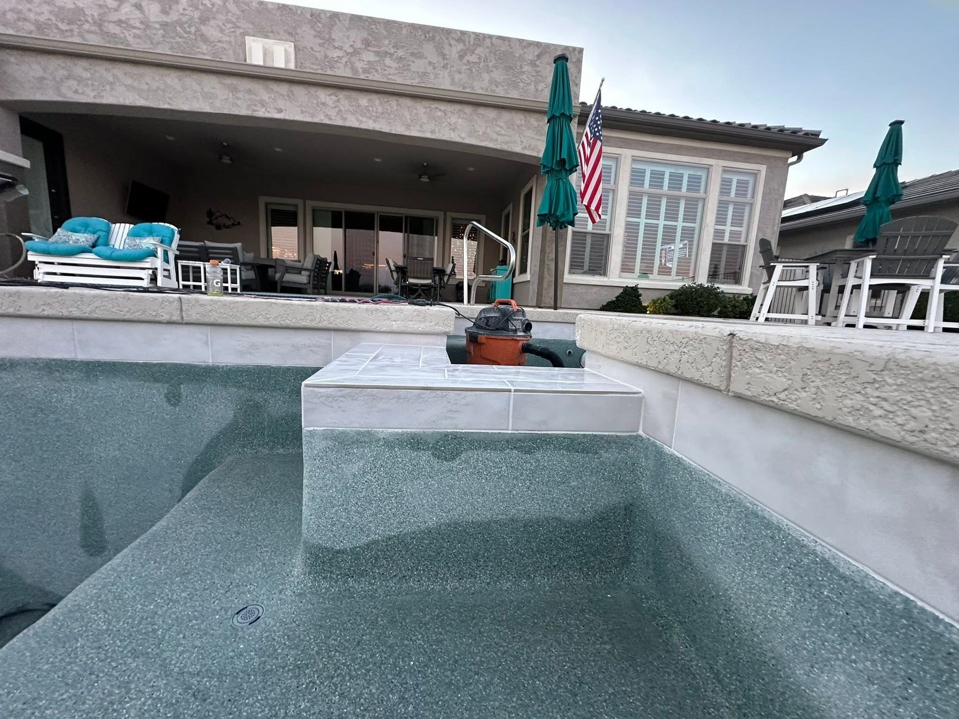 Backyard pool with a built-in fire pit, patio chairs, and umbrellas beside a house