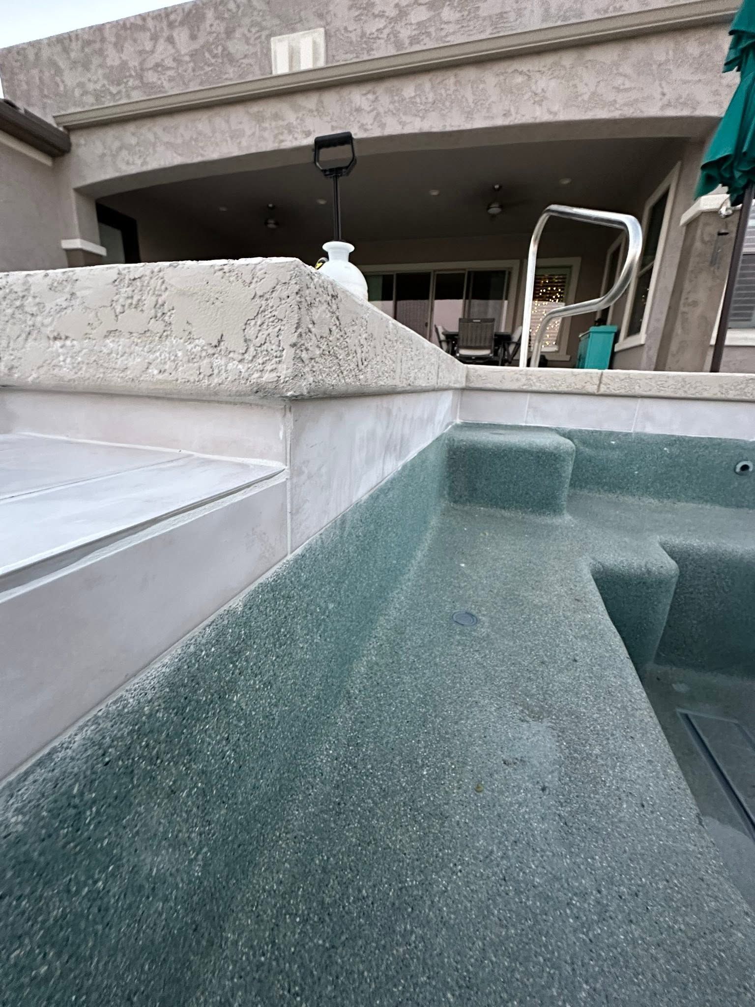 Close-up of a hot tub edge with clear water beside a covered patio and outdoor furniture.