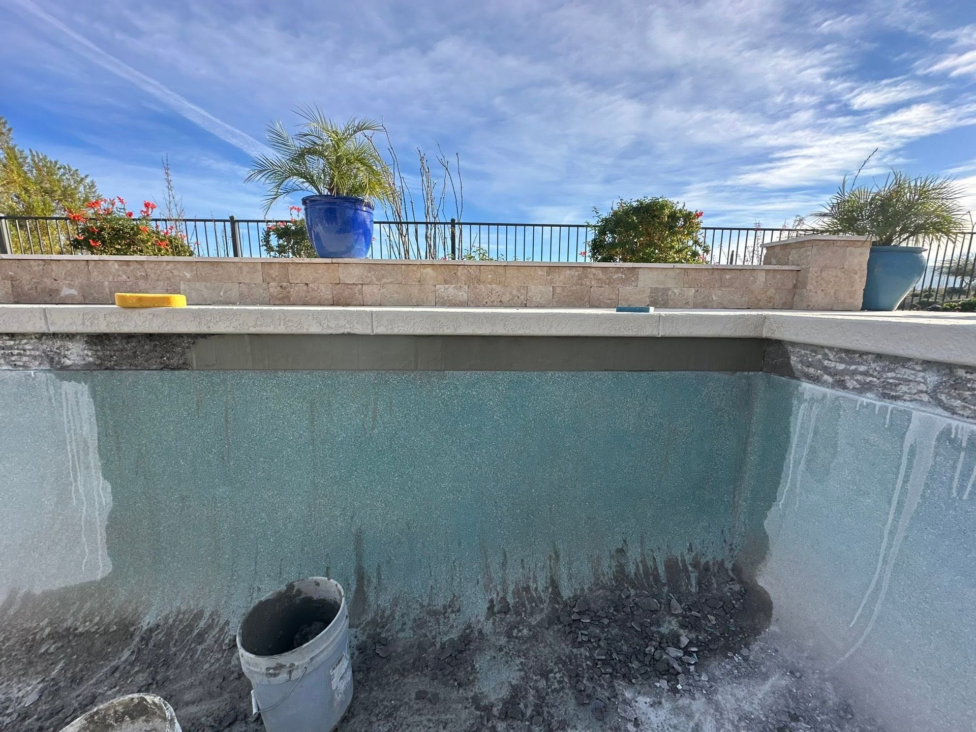Empty backyard pool being renovated, with exposed pool walls and a drain pipe under a bright blue sky.