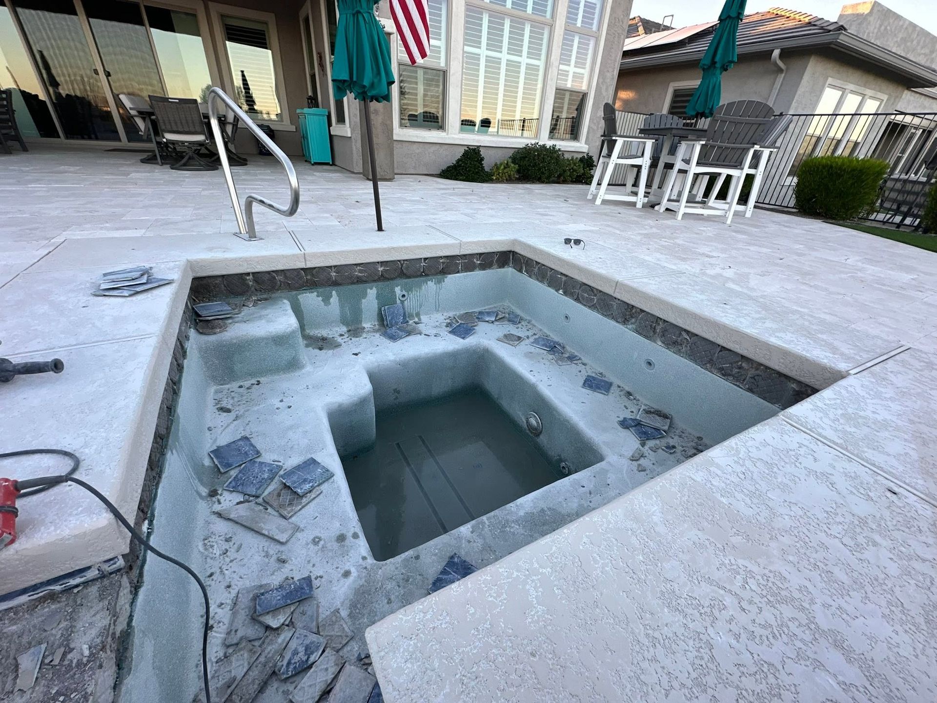 Empty hot tub on a patio with tile and lounge chairs in the background