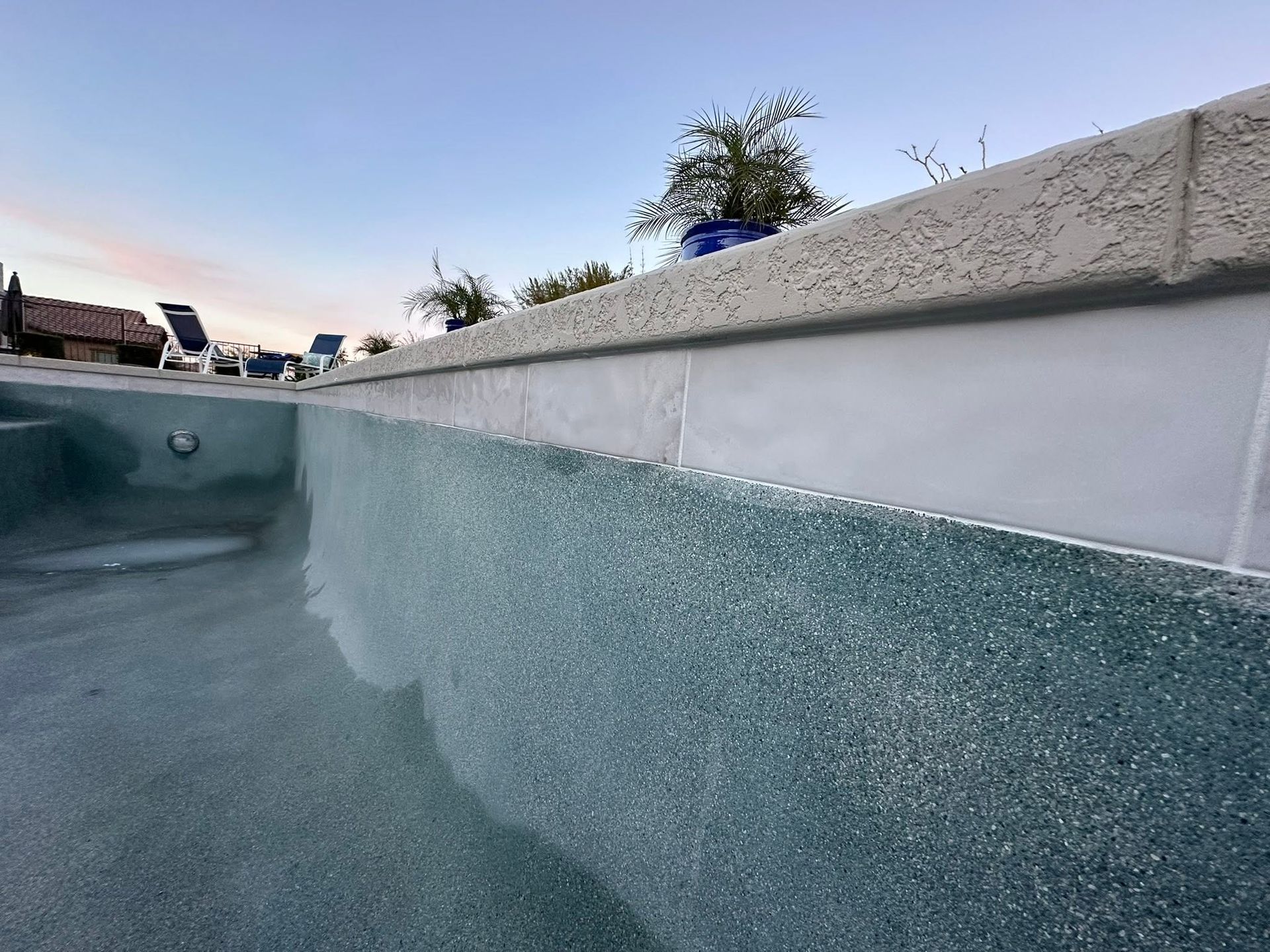 Empty outdoor swimming pool with blue-green waterline tiles and a white coping edge at sunset