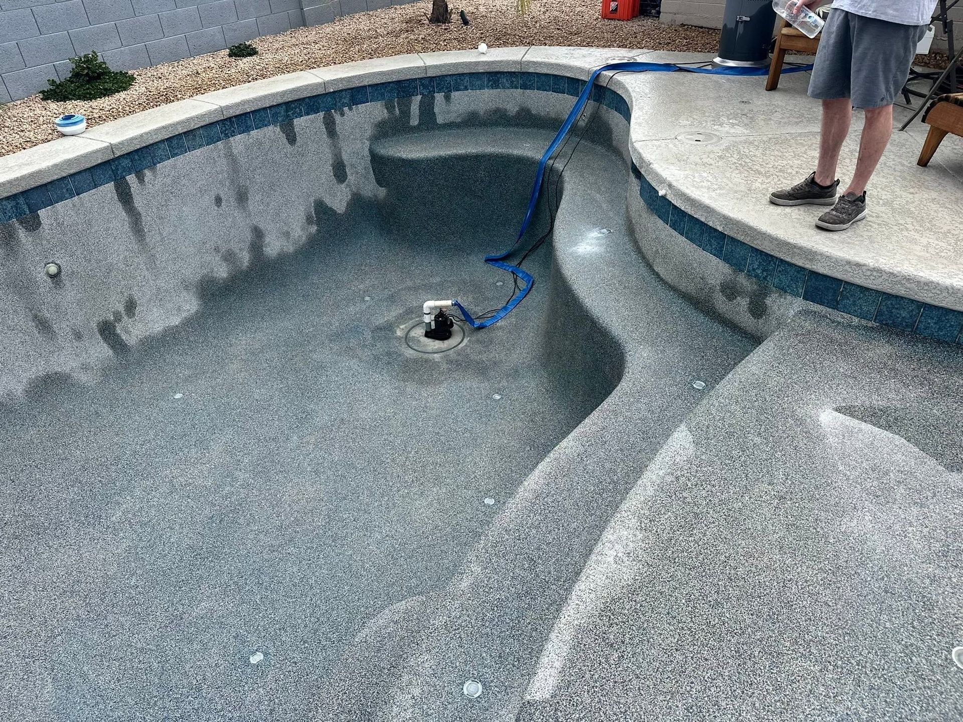 Empty drained swimming pool with a blue hose and two people standing on the deck