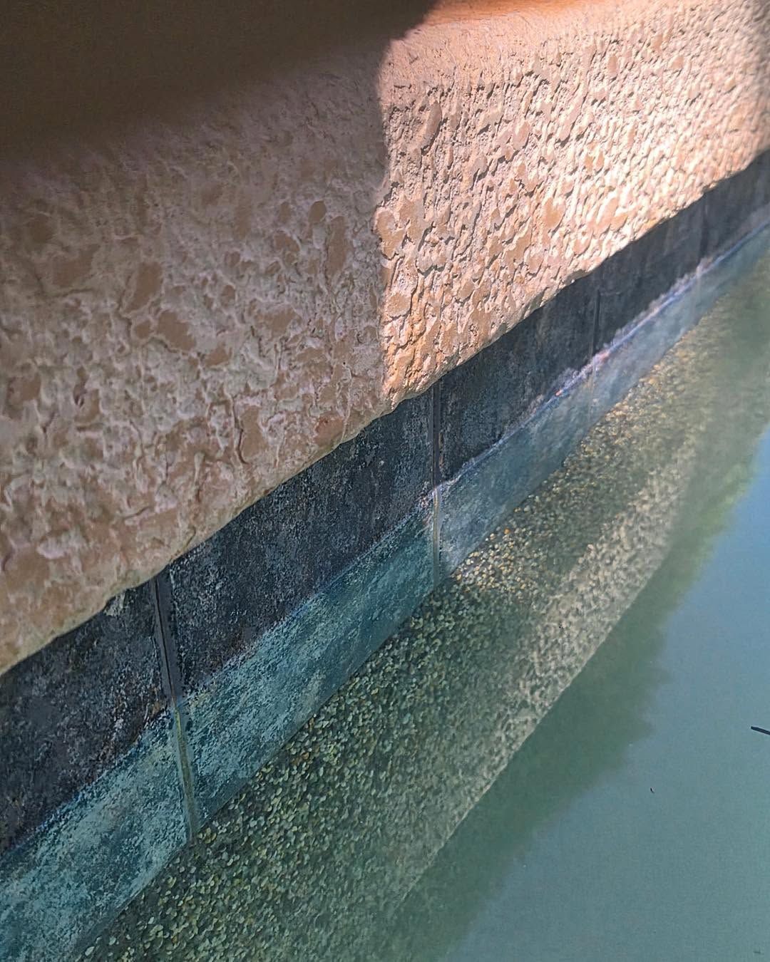 Sunlit textured wall beside a blue-green pool edge with rippling water