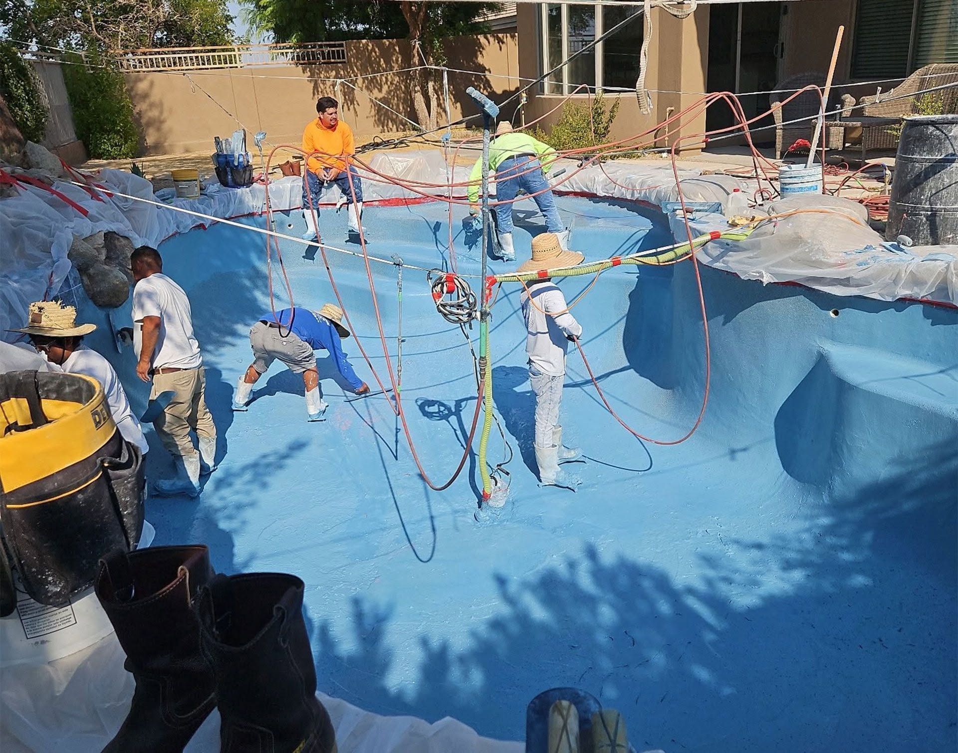 Workers painting a large blue swimming pool with ropes and tools around the edges