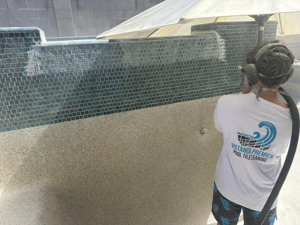Worker tiling a pool wall with blue mosaic tiles and beige plaster below