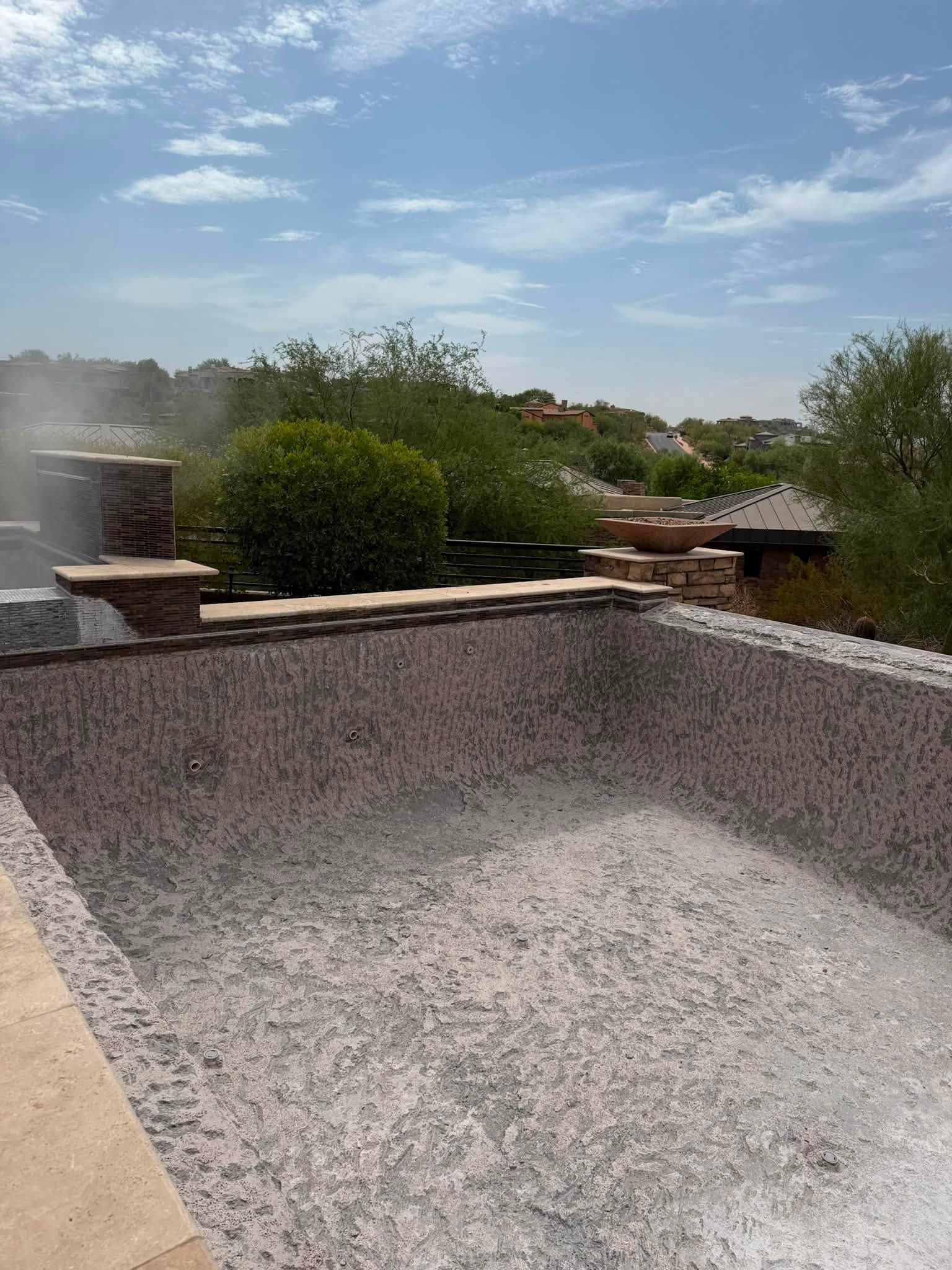 Empty rooftop pool under a blue sky, with greenery and rooftops in the background