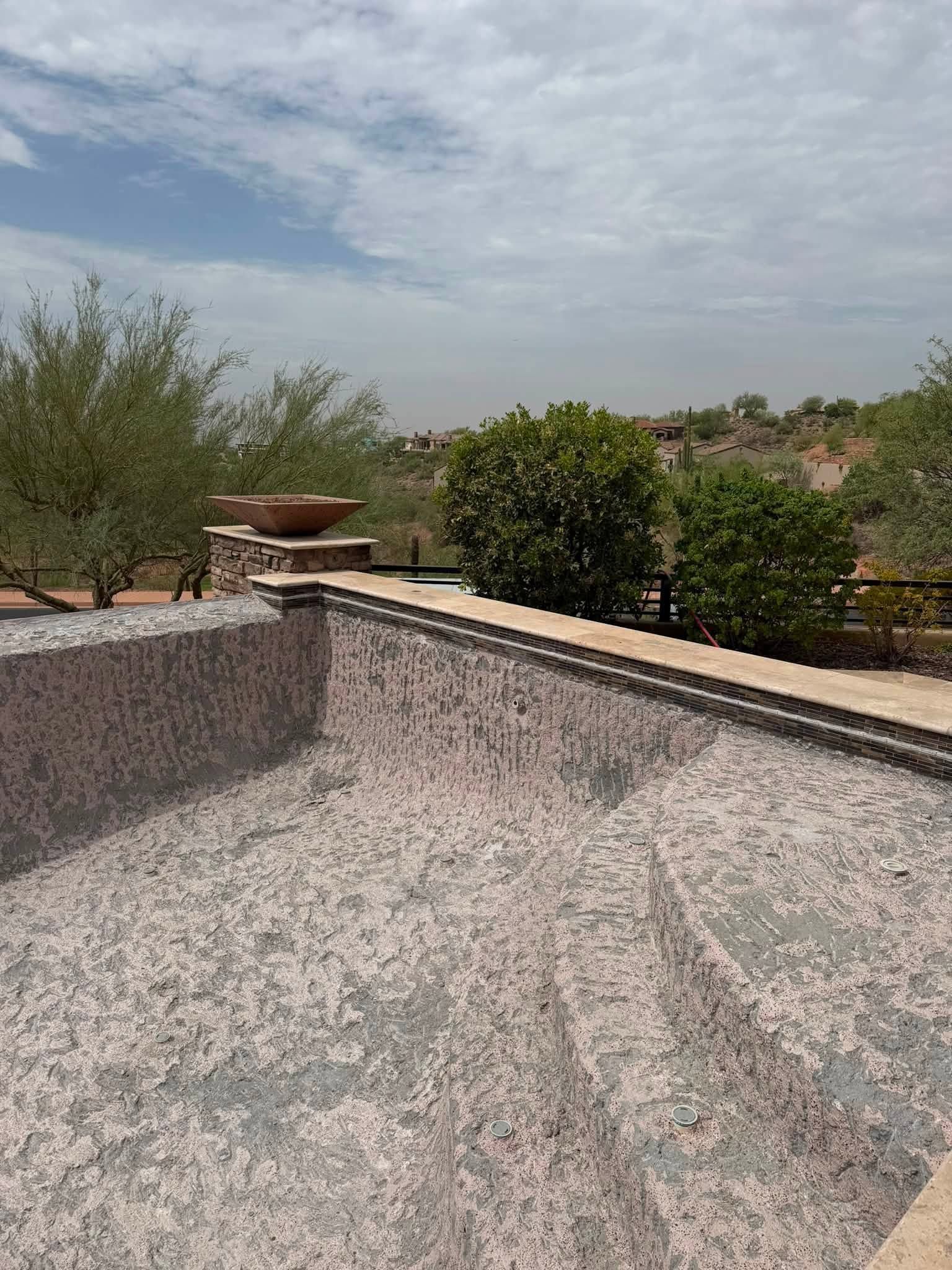 Empty concrete pool under a cloudy sky with trees and rooftops in the background