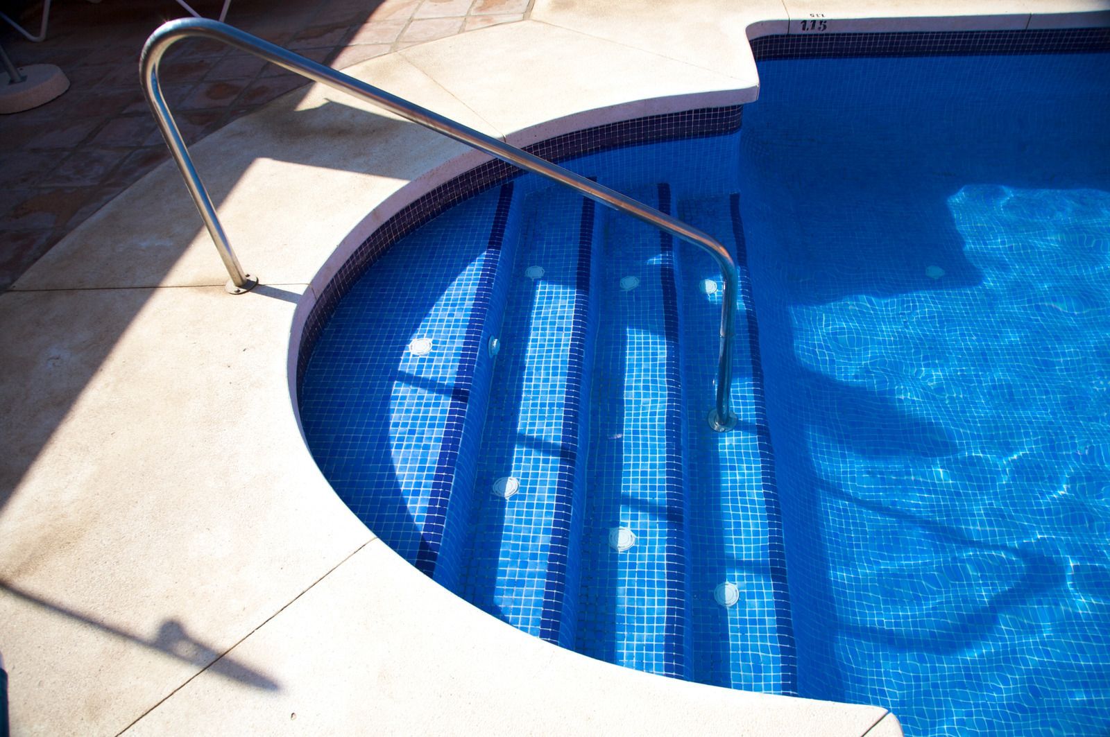 Curved pool ladder at the edge of a blue swimming pool on a sunlit patio