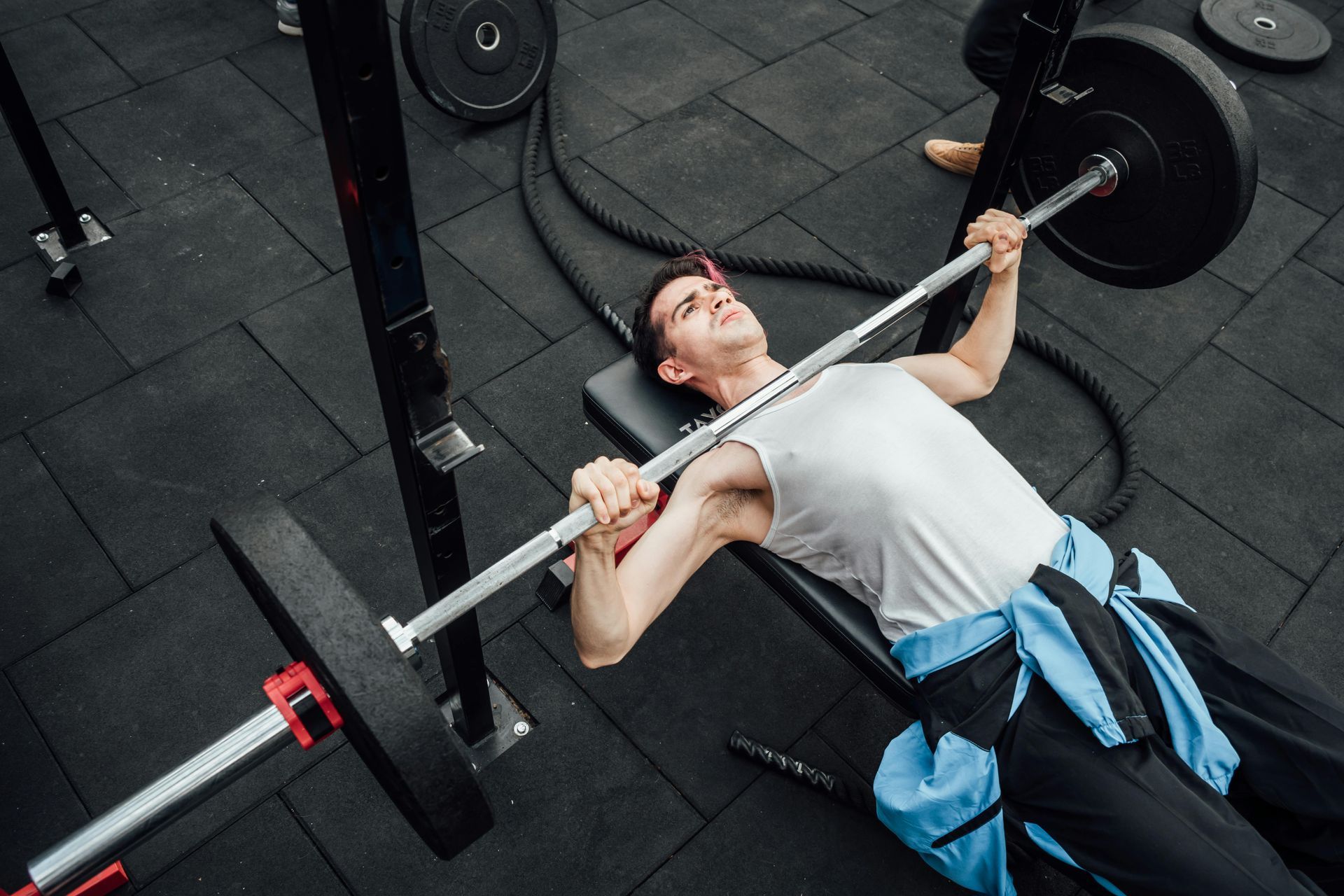 Man bench presses a barbell in a gym, with black weights and flooring.