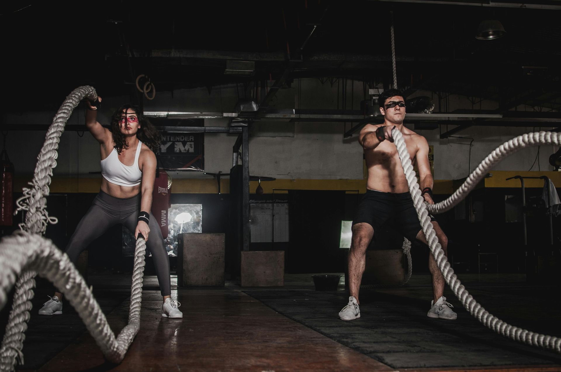 Two people exercising with battle ropes in a dimly lit gym.