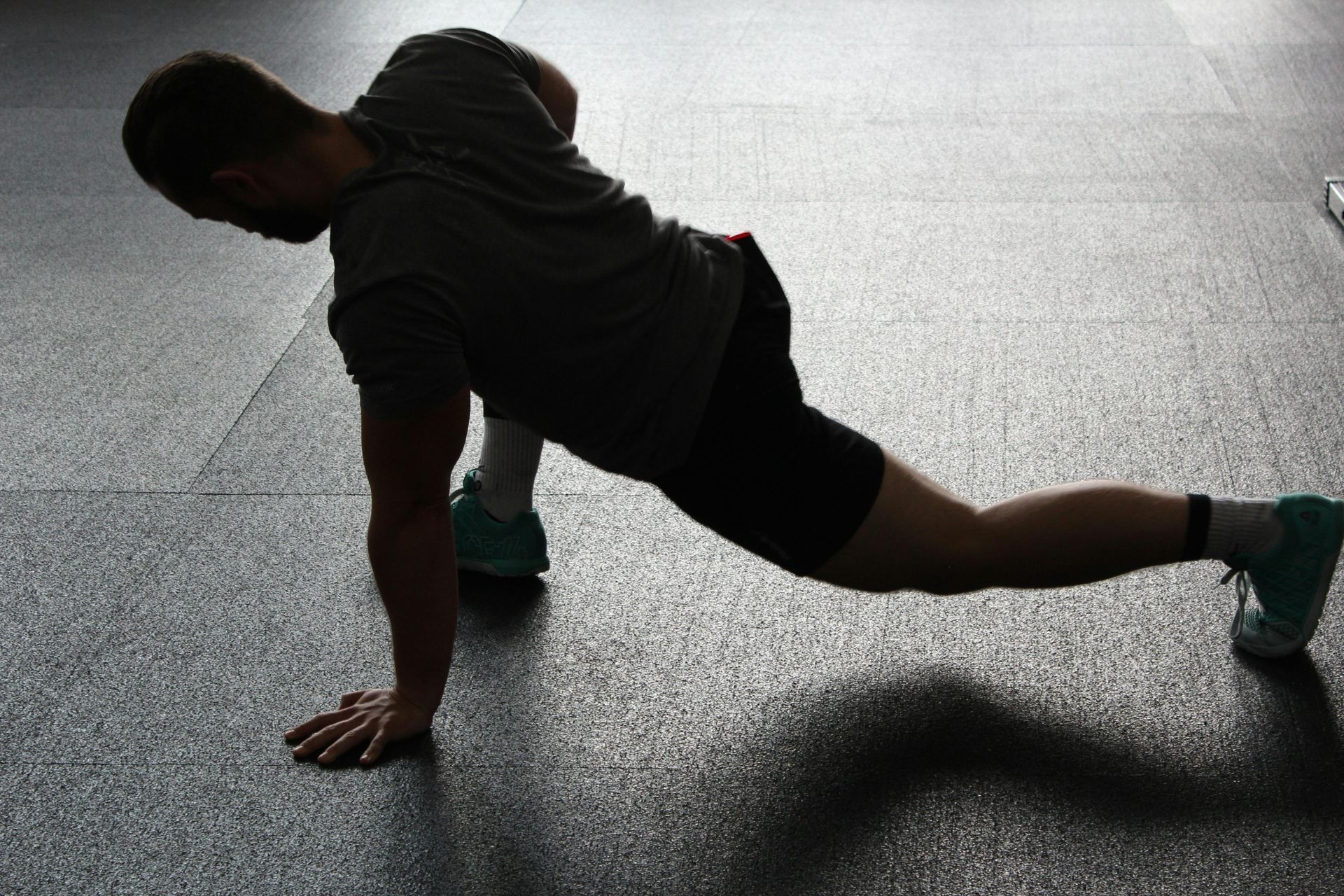 Man in athletic wear stretching on a dark floor, twisting torso towards the upraised arm.