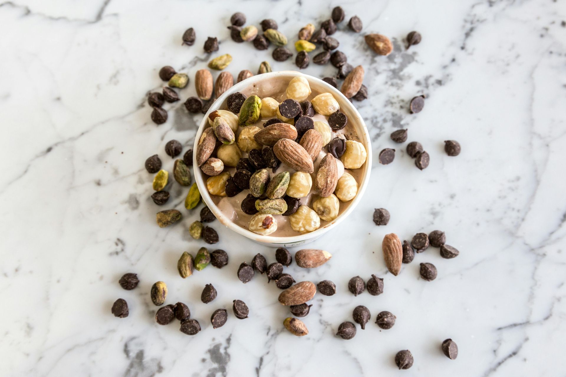 Bowl of mixed nuts and chocolate chips on a marble surface.