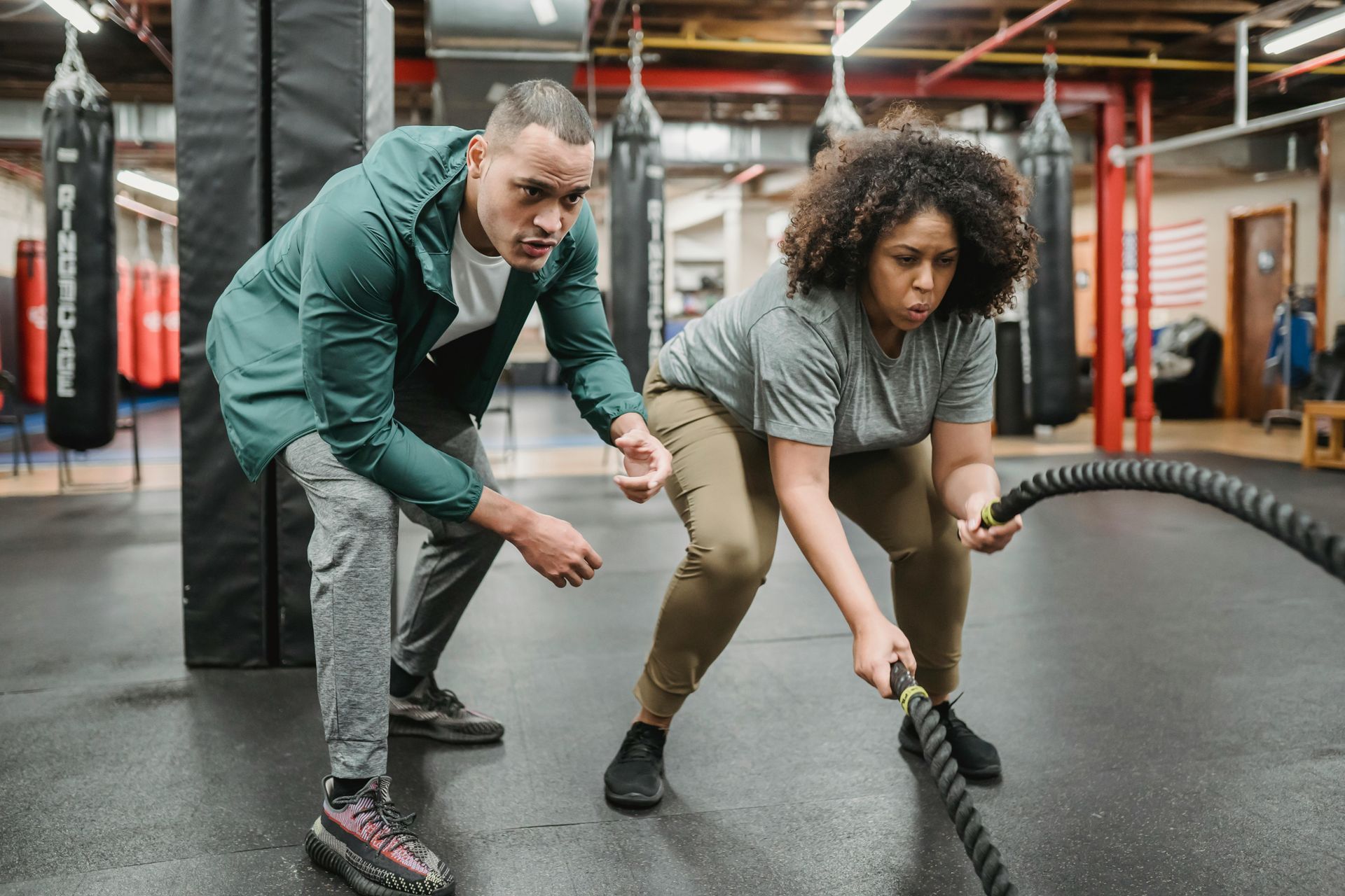 Man and woman exercising with battle ropes in gym, man coaching.