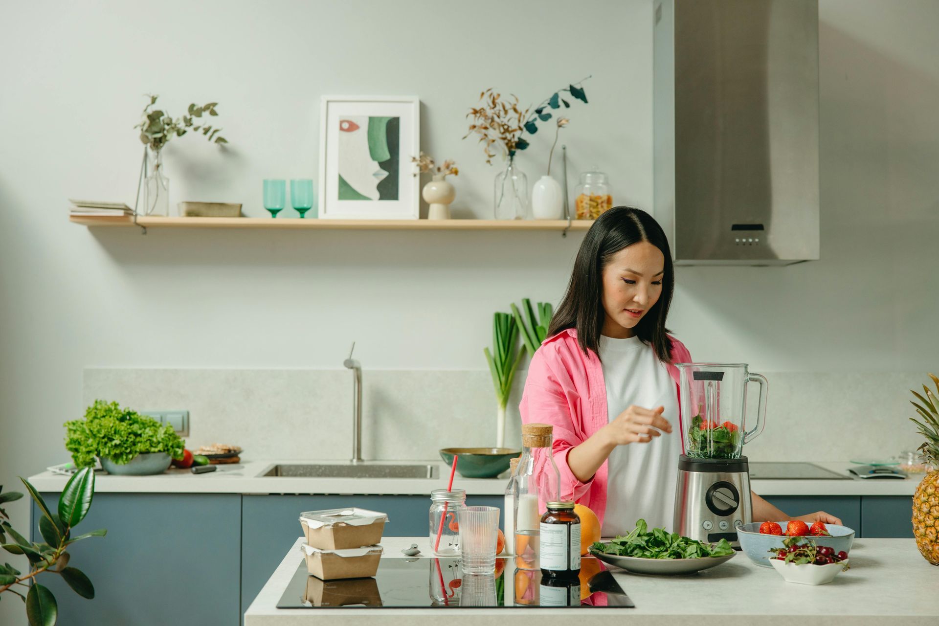 Woman making a smoothie in a bright kitchen with fresh produce.