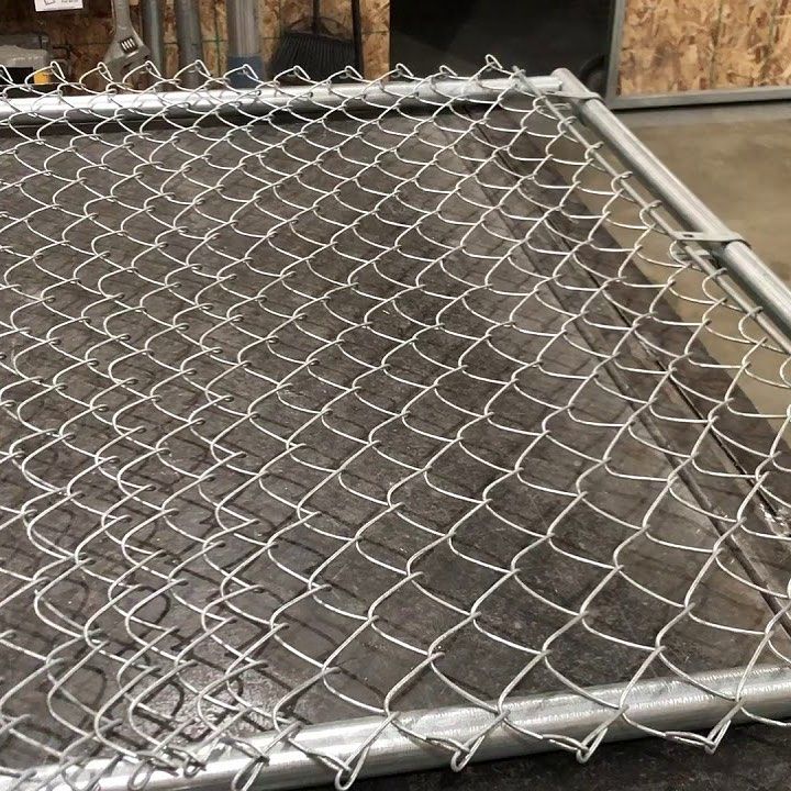 Close-up of a metal chain-link fence panel. Silver wire forms a diamond pattern within a gray metal frame.