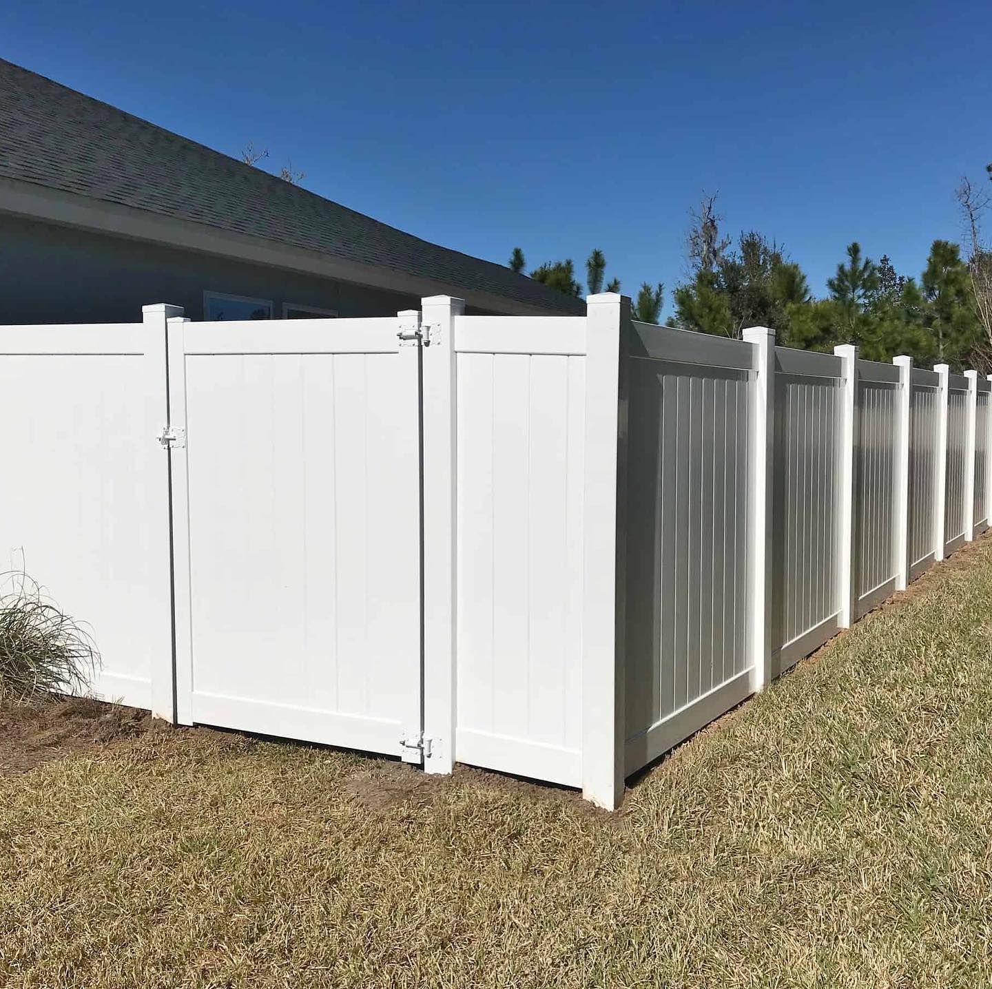 White vinyl fence with gate in front of a house under a clear, blue sky.