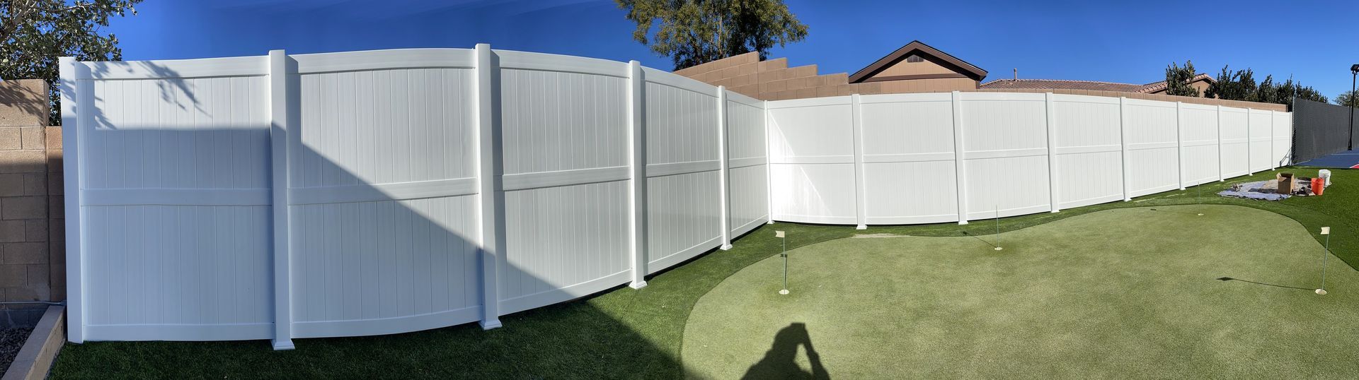 White vinyl fence bordering a green, artificial grass yard; blue sky in the background.