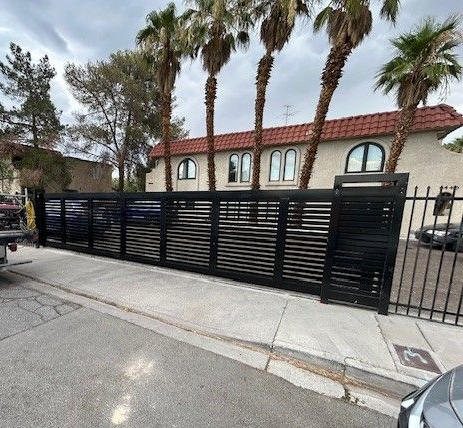 Black wrought iron fence with scrolled and pointed accents, blurring a green bush and building.