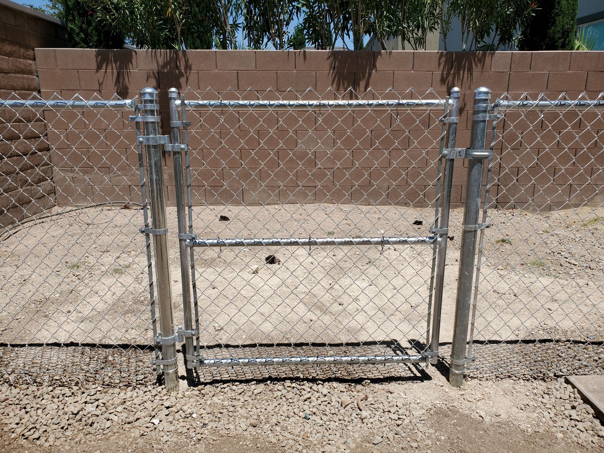 Person in plaid shirt holding rolled chain-link fence, wearing red gloves, outdoors.