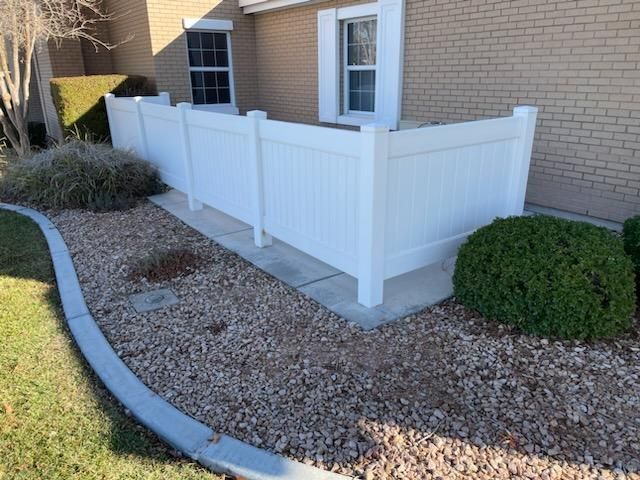 Brown composite fence with perforated top section, set outdoors with trees in background.