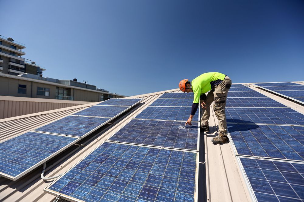 Technician inspecting solar panels on a rooftop under clear blue skies.
