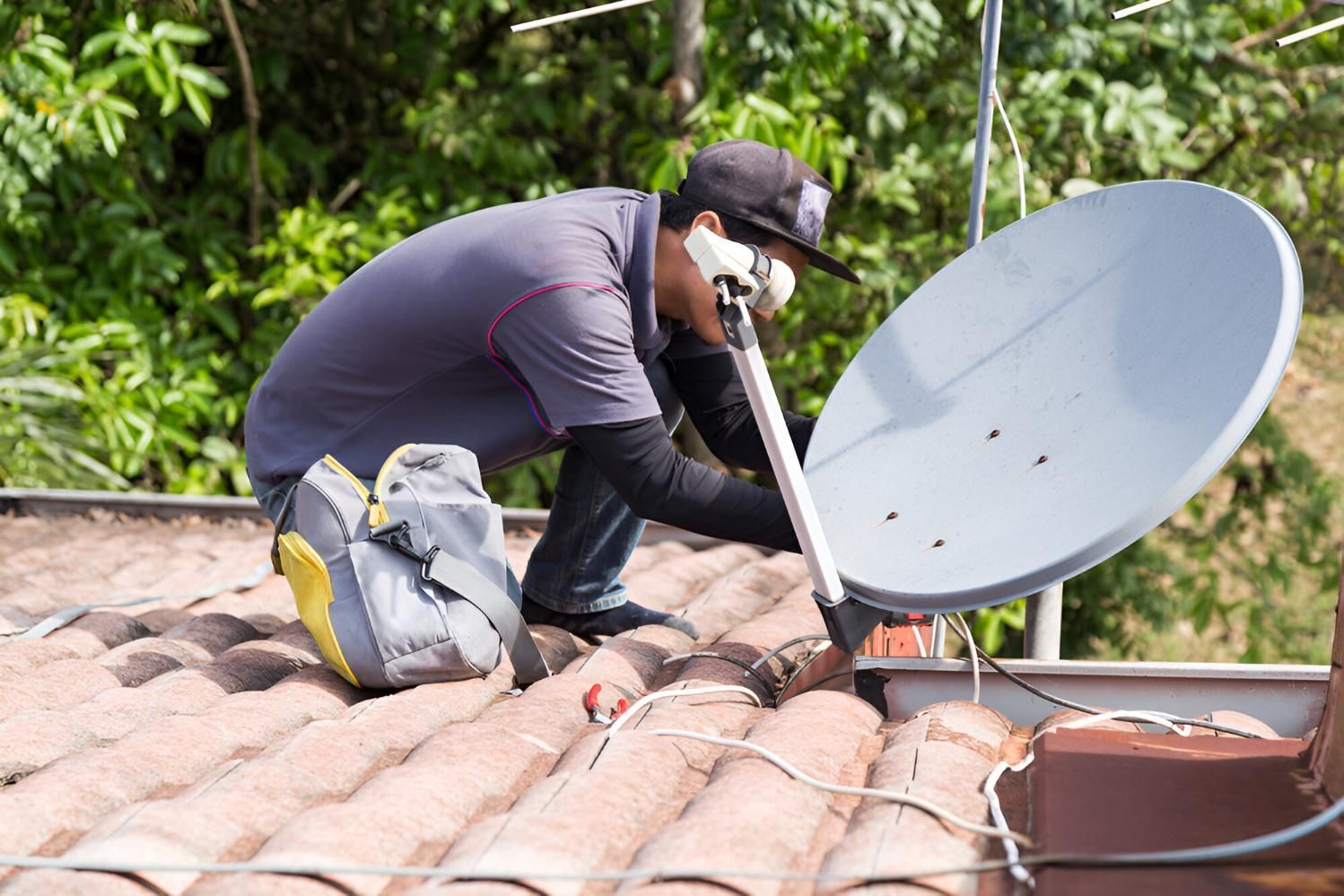 A Man Is Installing a TV Antenna Dish on The Roof of A House — Robbie McDonald Electrical in Golden Beach, QLD