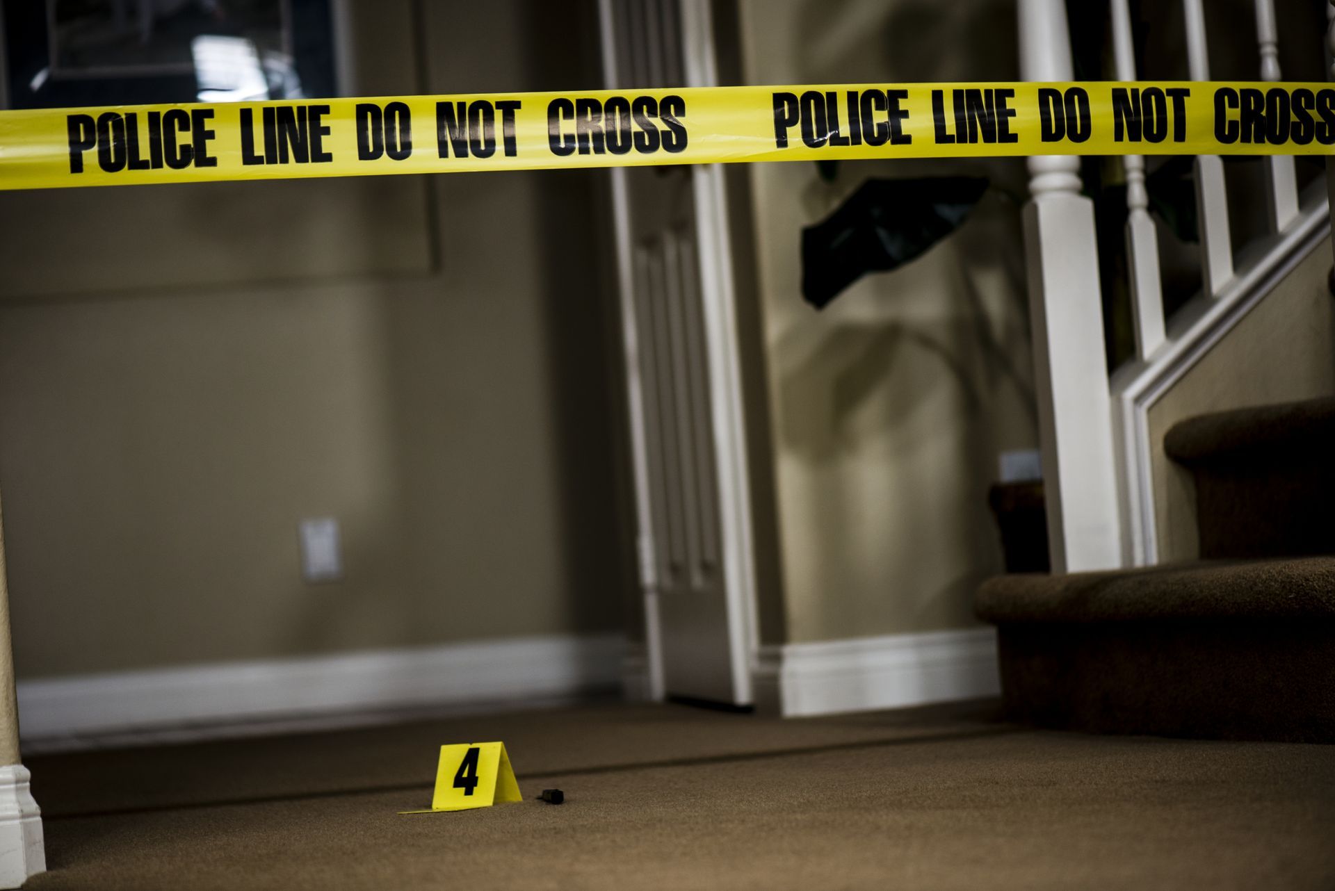 Police tape blocks a hallway with a yellow evidence marker on the floor.